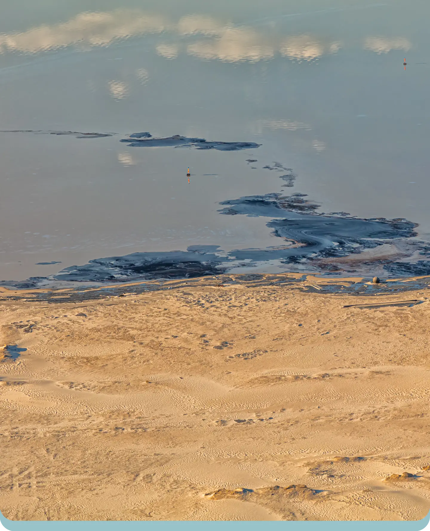 A body of water with sand and clouds in the background.